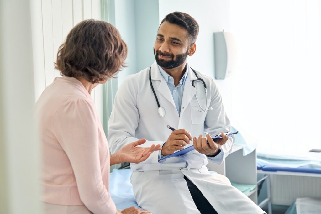 Indian male doctor physician consulting senior patient filling medical form.